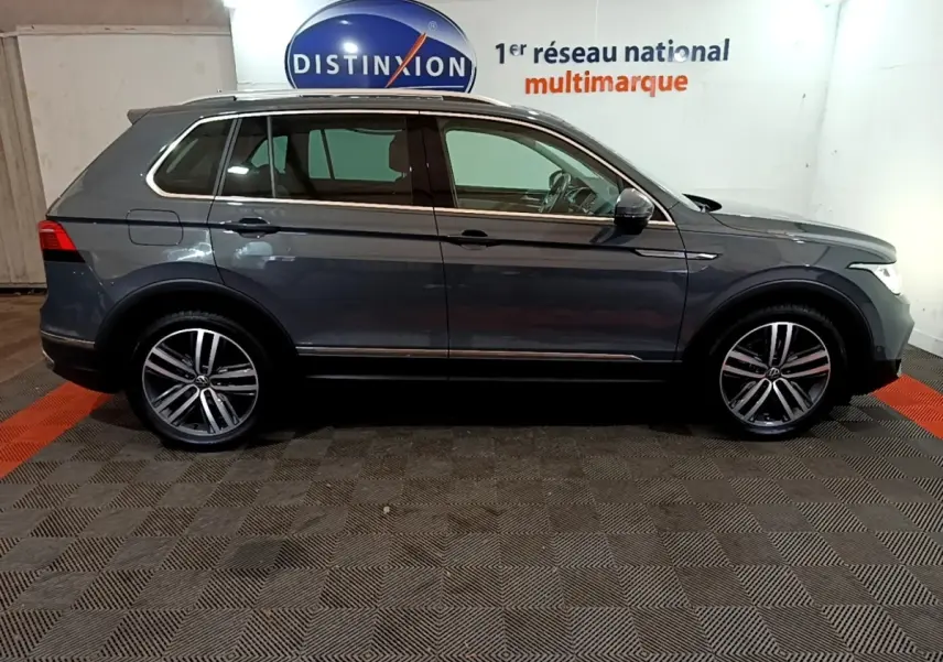 Vue de profil côté gauche d'un Volkswagen Tiguan gris clair 2022 stationné en intérieur avec jantes alliage.