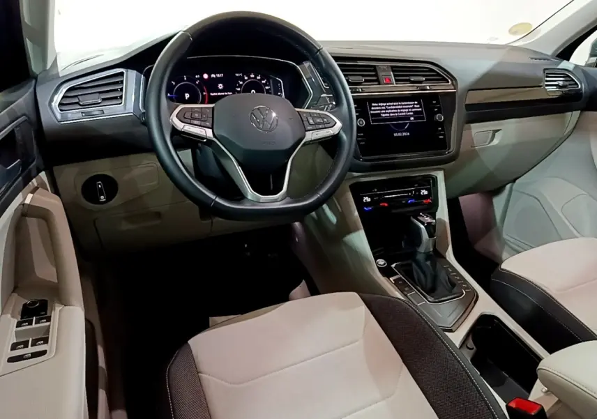 Vue intérieure avant du Volkswagen Tiguan 2.0 TDI gris clair, volant cuir multifonctions et écran tactile central.
