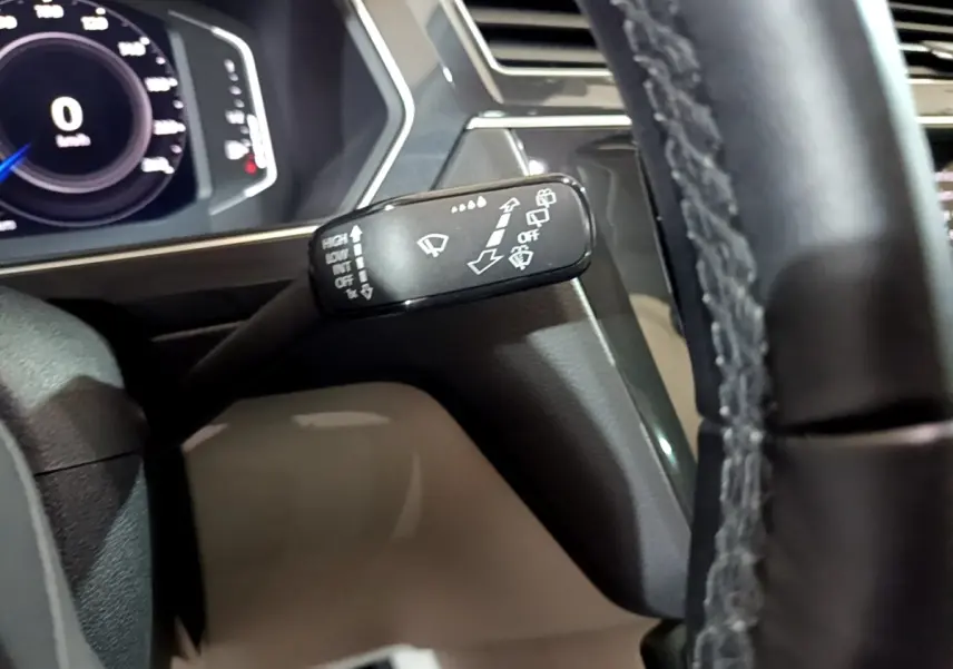 Gros plan sur la manette d’essuie-glace à gauche du volant cuir dans l’habitacle du Volkswagen Tiguan gris clair.