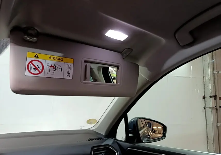 Vue intérieure côté conducteur du Volkswagen Tiguan gris clair 2022, avec pare-soleil baissé et miroir intégré allumé.