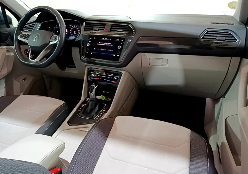 Vue intérieure avant du Volkswagen Tiguan 2.0 TDI gris clair, avec tableau de bord moderne et écran tactile central.