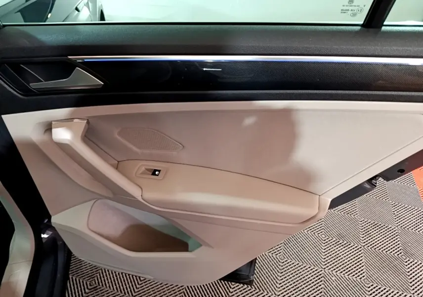 Vue intérieure côté gauche de la porte beige du Volkswagen Tiguan 2022 avec bande décorative noire et bouton de lève-vitre.