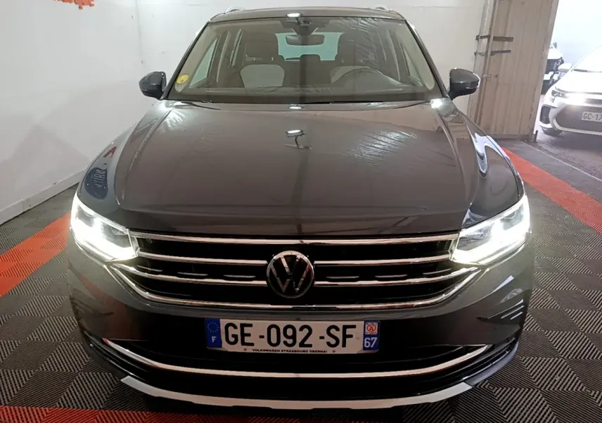 Vue avant d'un Volkswagen Tiguan gris clair avec phares LED allumés et calandre chromée brillante.