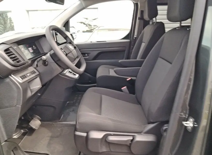 Vue intérieure côté conducteur du Citroën Jumpy gris titane, montrant les sièges avant avec accoudoirs et tableau de bord.