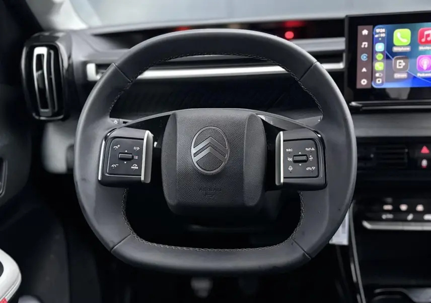 Vue frontale du volant noir de la Citroën C3 2025 avec commandes intégrées et écran tactile multimédia en arrière-plan.