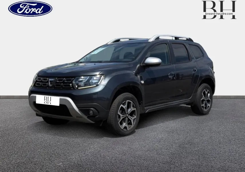 SUV Dacia Duster gris Comète métallisé vu en 3/4 avant droit avec barres de toit et jantes alu noires.