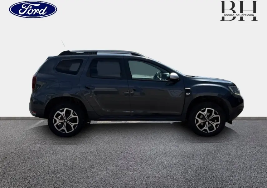Profil côté gauche du Dacia Duster 2020 gris Comète métallisé avec jantes alu et barres de toit visibles.