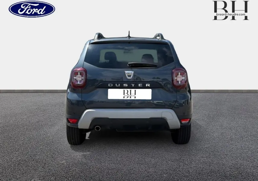 Vue arrière du Dacia Duster gris Comète métallisé avec barres de toit et sortie d'échappement chromée visible.