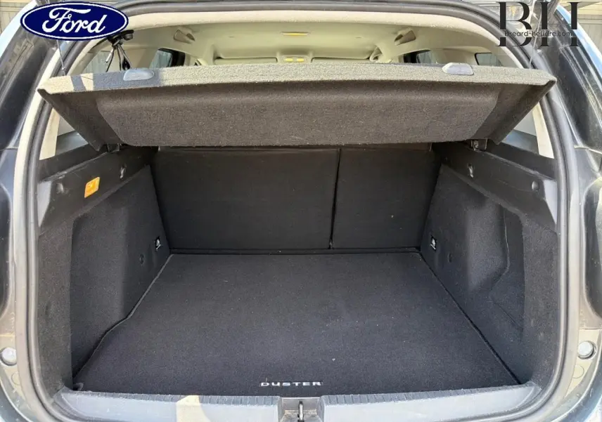 Coffre ouvert vu de l'arrière d'un Dacia Duster gris avec tapis de coffre noir marqué Duster.