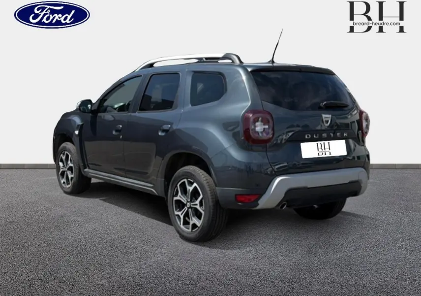 Vue 3/4 arrière droite du Dacia Duster gris Comète métallisé avec barres de toit et jantes alu distinctives.