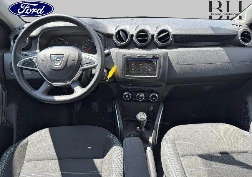 Intérieur avant du Dacia Duster 2020 en tissu gris, vue centrée sur le tableau de bord et la boîte manuelle.