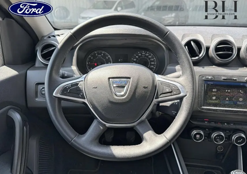 Vue intérieure centrée sur le volant Dacia du Duster 2020, avec commandes multifonctions et tableau de bord visible.
