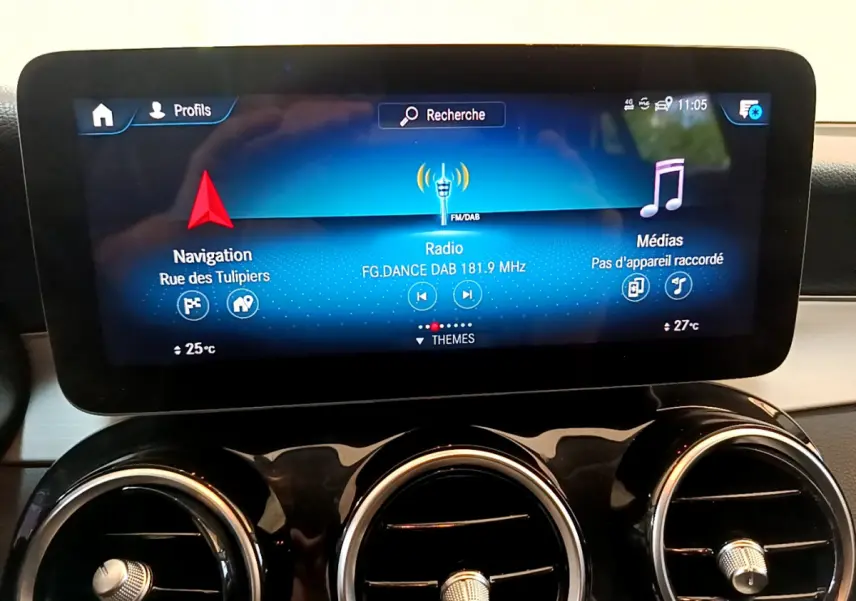 Écran tactile central affichant navigation, radio et médias, avec trois aérateurs ronds chromés en dessous dans un Mercedes GLC 2021.