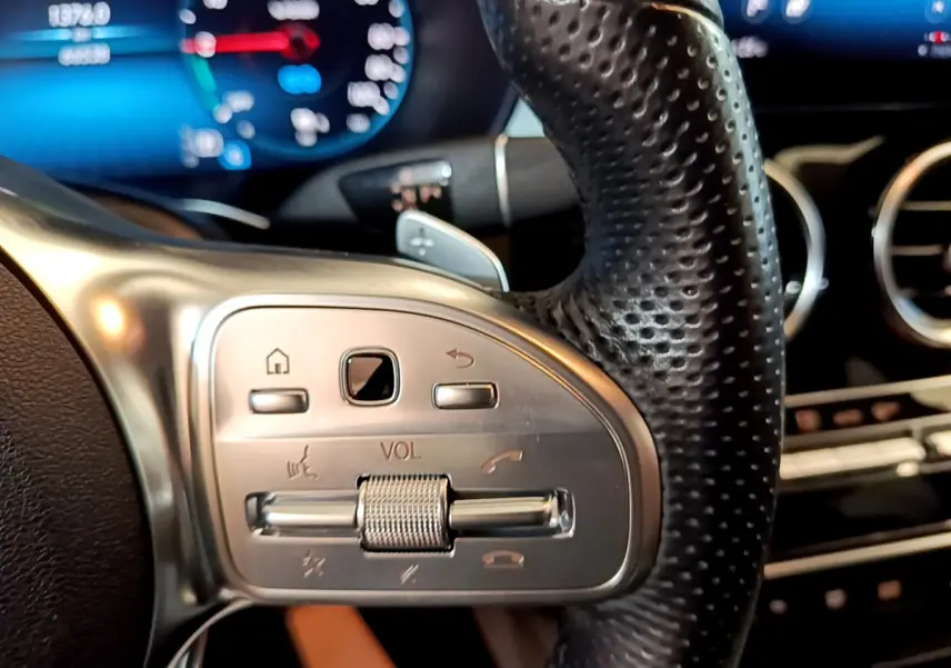 Gros plan sur les commandes du volant cuir perforé du Mercedes GLC 300 E AMG Line 2021, tableau de bord numérique en arrière-plan.