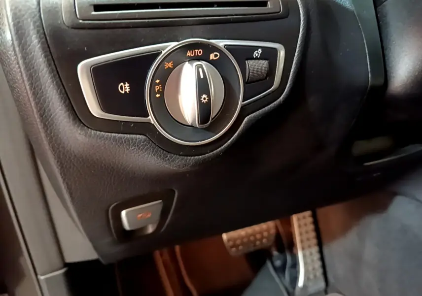 Gros plan sur la commande des phares et le bouton de frein de stationnement dans l'habitacle noir du Mercedes GLC 300 E AMG Line.