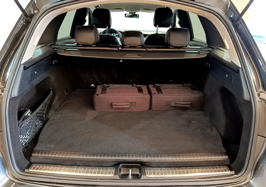 Coffre ouvert du Mercedes GLC 300 E AMG Line gris foncé, avec deux valises noires et banquette arrière visible.