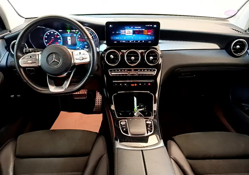 Vue intérieure avant du Mercedes GLC 300 E AMG Line 2021, tableau de bord noir avec écran tactile et volant multifonctions cuir.