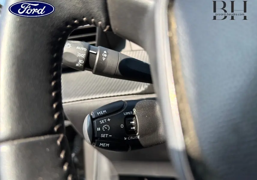 Gros plan sur la commande de régulateur de vitesse au volant d’une Peugeot 208 gris Platinium, intérieur visible.