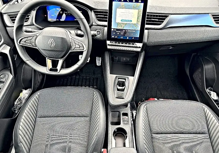 Vue intérieure avant du Renault Symbioz 2026 avec tableau de bord noir, écran tactile vertical et sièges en tissu gris.