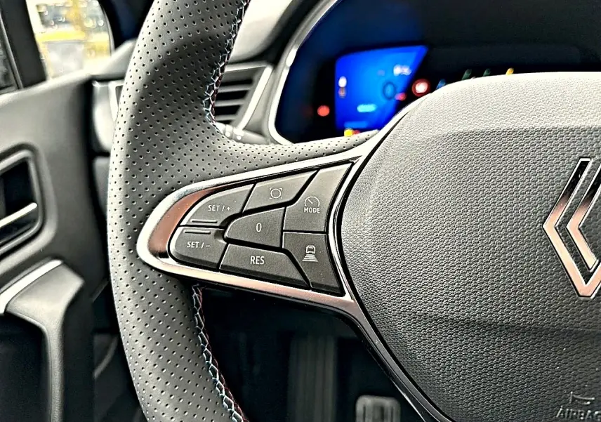 Gros plan sur le volant perforé noir de la Renault Symbioz 2026 avec commandes multifonctions côté gauche et tableau de bord bleu flou.