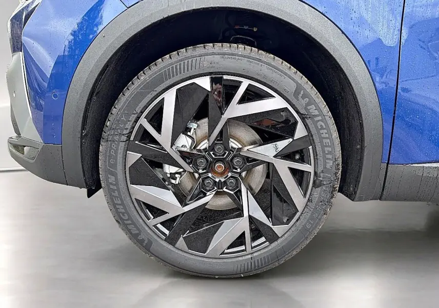 Gros plan sur la roue avant gauche du Renault Symbioz bleu iron avec jante alu au design géométrique noir et argent.