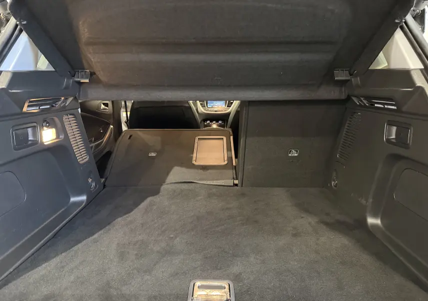 Vue intérieure du coffre ouvert de l’Opel Grandland X blanc, avec banquette arrière partiellement rabattue et cache-bagages relevé.