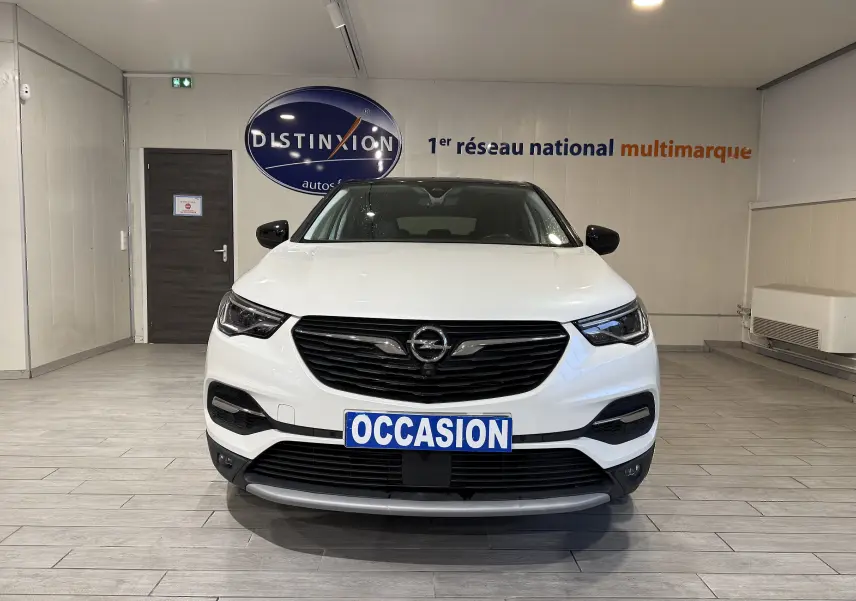 Vue frontale d'un Opel Grandland X blanc avec calandre noire et plaque "OCCASION" en intérieur showroom.