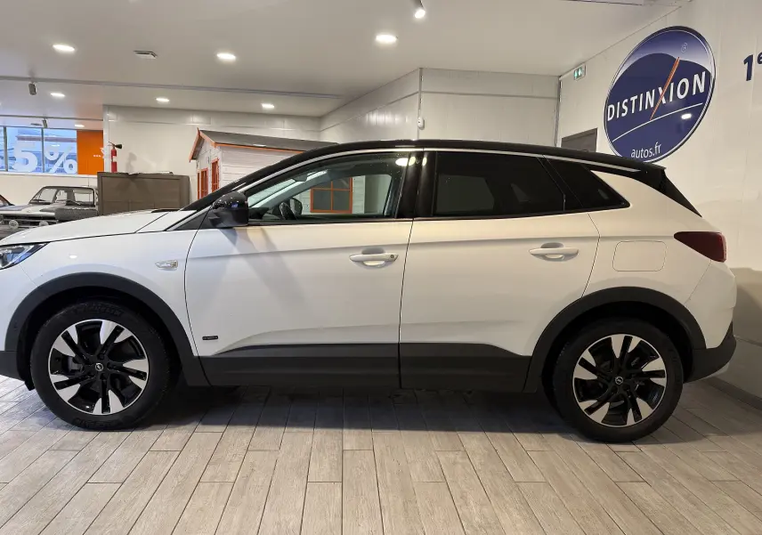 Vue de profil côté gauche d’un Opel Grandland X blanc avec toit noir et jantes bicolores en intérieur showroom.