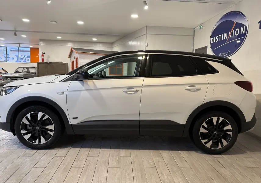 Opel Grandland X blanc en profil droit, avec jantes noires et toit noir contrastant en intérieur showroom.