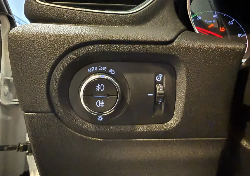 Gros plan sur le panneau de commande des phares noir à gauche du tableau de bord d’un Opel Grandland X blanc.