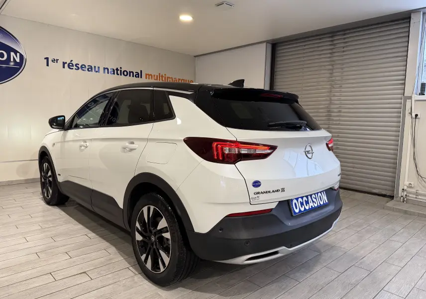 Vue 3/4 arrière droite d'un Opel Grandland X blanc avec toit noir, feux LED et jantes alliage noires en showroom.