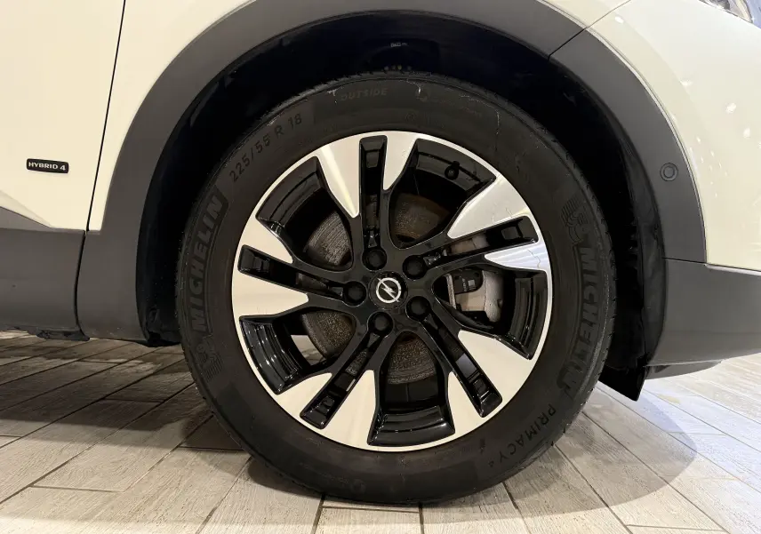 Gros plan sur la roue avant droite d’un Opel Grandland X blanc avec jante alliage bicolore et badge Opel au centre.