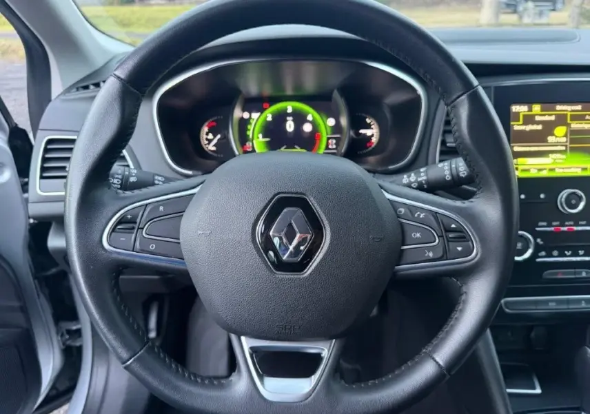 Vue centrée sur le volant noir de la Renault Mégane Business, avec tableau de bord numérique et écran tactile en arrière-plan.