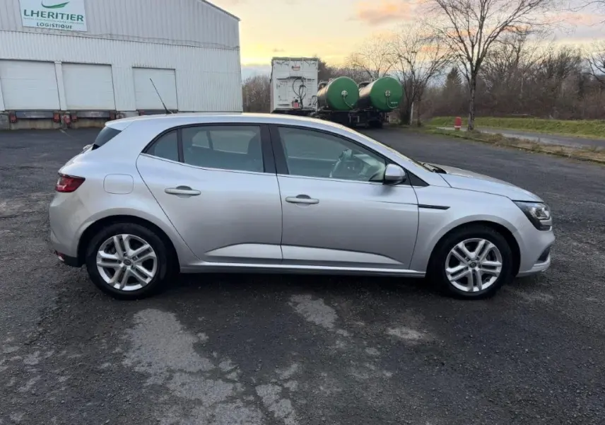 Profil côté gauche d'une Renault Mégane Business gris alu, avec jantes alliage et lignes épurées visibles.