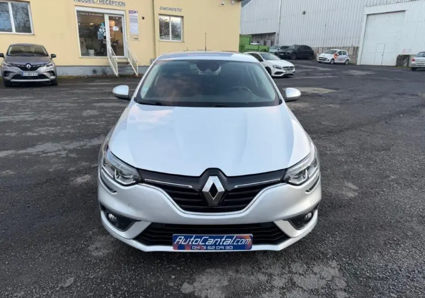 Vue avant d'une Renault Mégane Business gris alu avec calandre noire et phares LED, stationnée devant un bâtiment jaune.