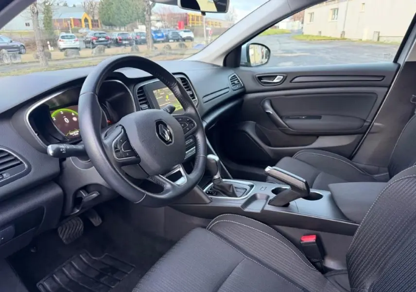 Vue intérieure côté conducteur de la Renault Mégane Business gris alu, avec tableau de bord numérique et console centrale moderne.