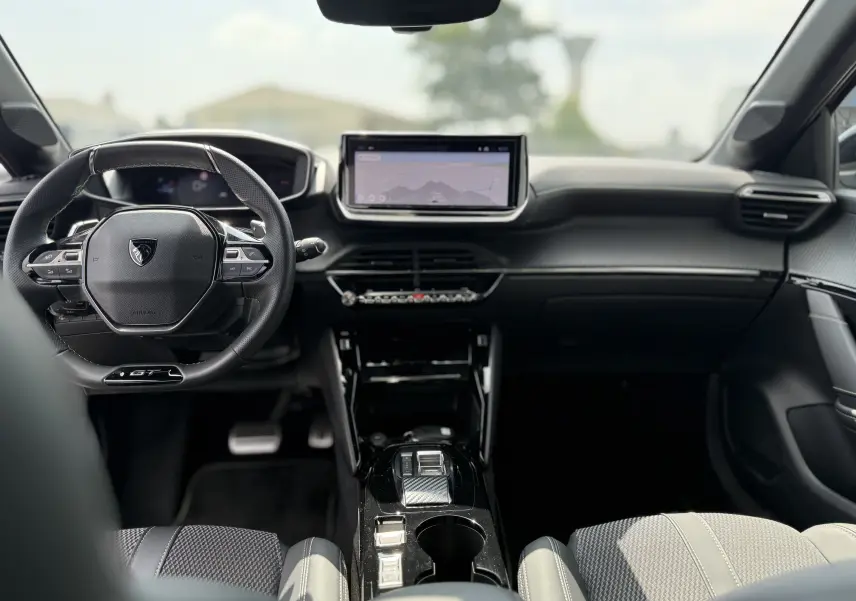 Intérieur de la Peugeot 208 HYBRID 145 GT 2024, vue frontale du tableau de bord et volant compact noir avec écran tactile central.