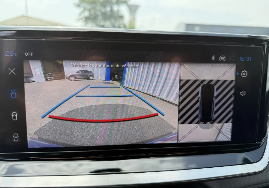 Vue écran caméra de recul et vue 360 du Peugeot 208 gris Artense stationné près d'un bâtiment industriel.