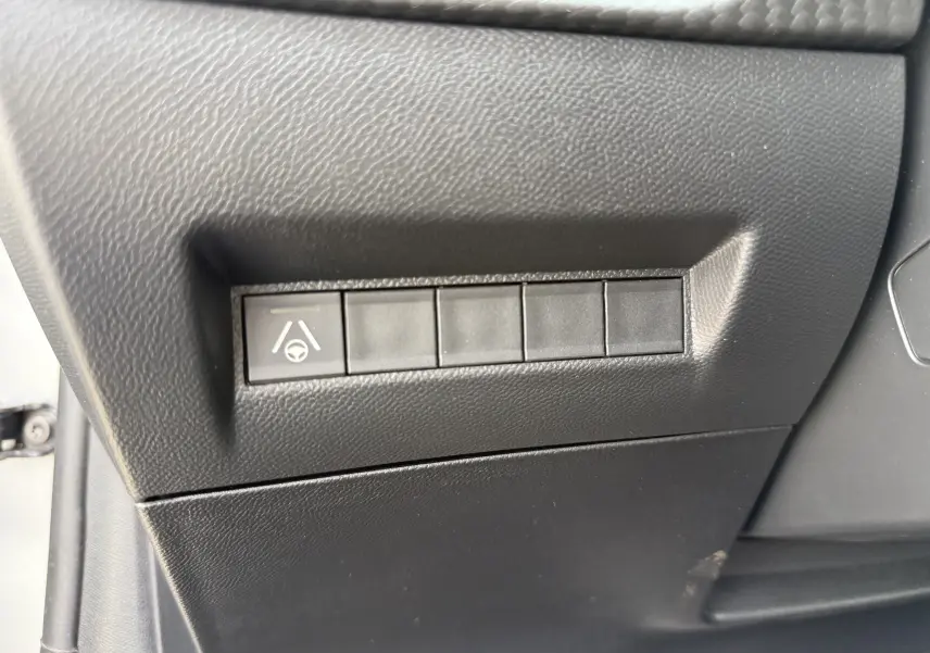 Gros plan sur le panneau de commandes latéral noir mat avec bouton d'assistance au maintien de voie dans une Peugeot 208 gris Artense.