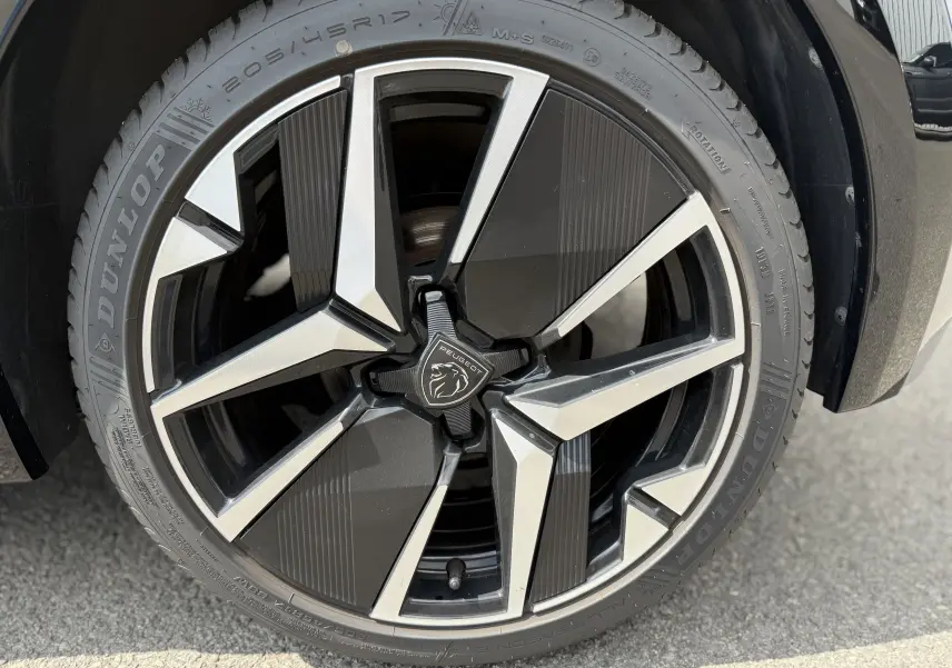 Gros plan sur la jante noire et argentée de la Peugeot 208 HYBRID 145 GT E-DCS6 gris Artense de 2024.