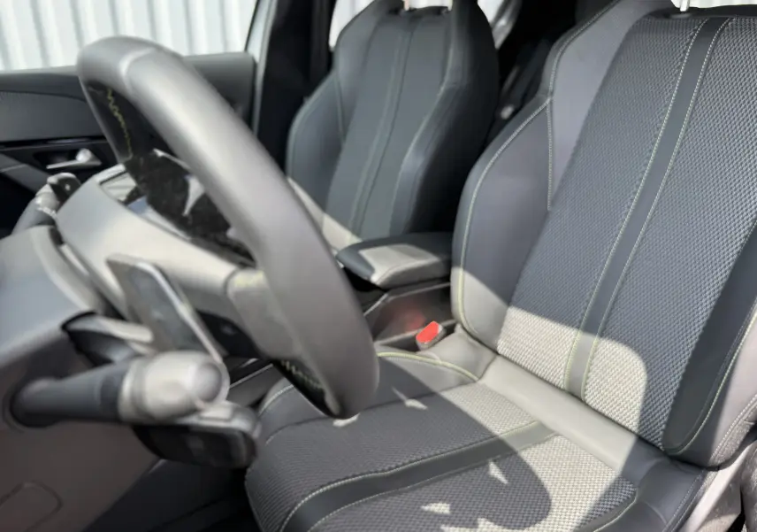 Intérieur de la Peugeot 208 HYBRID 145 GT en gris, vue rapprochée sur les sièges avant avec surpiqûres vertes.
