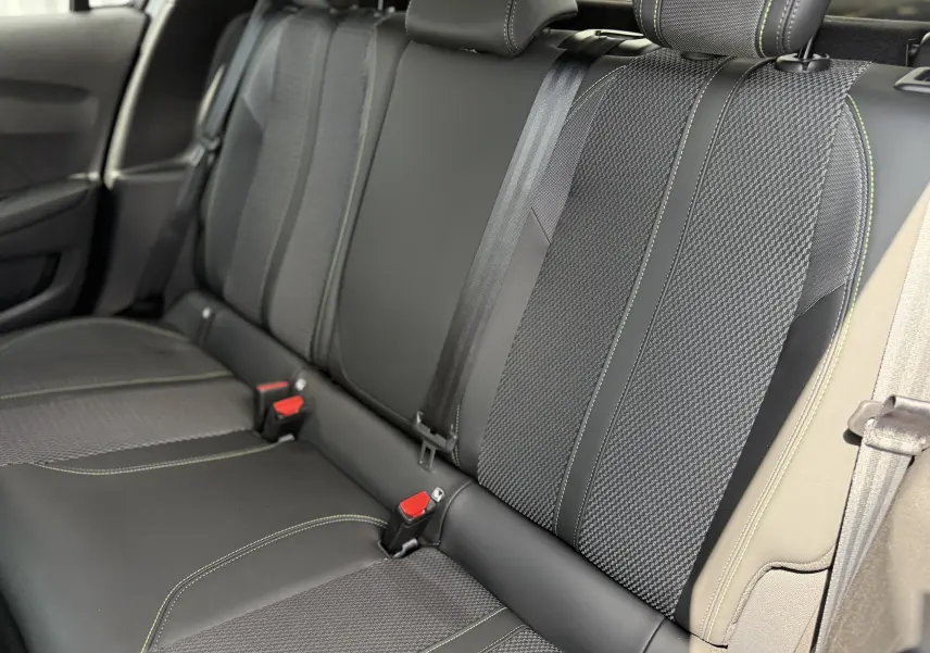 Vue intérieure de la banquette arrière de la Peugeot 208 Hybrid 145 GT E-DCS6 avec sellerie noire et surpiqûres vertes.