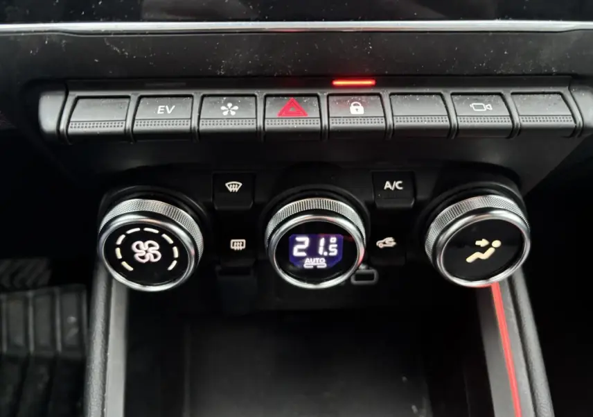 Vue rapprochée des commandes de climatisation et des boutons de fonction sur la console centrale de la Renault Clio rouge flamme.