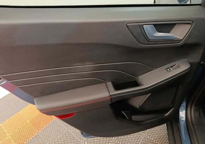 Gros plan sur la porte avant gauche intérieure noire avec surpiqûres rouges du Ford Kuga bleu 2024 St Line