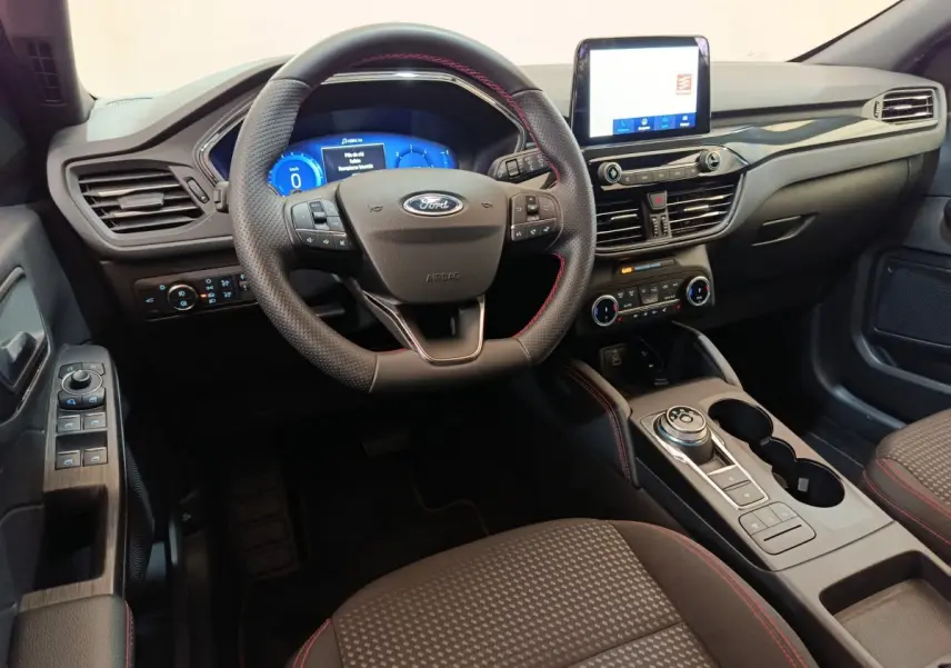 Vue intérieure avant du Ford Kuga 2024 St Line, tableau de bord noir avec écran tactile et volant cuir à surpiqûres rouges