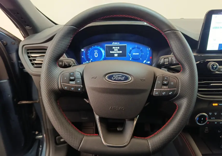 Vue rapprochée du volant en cuir noir avec surpiqûres rouges du Ford Kuga bleu 2024, tableau de bord digital visible.
