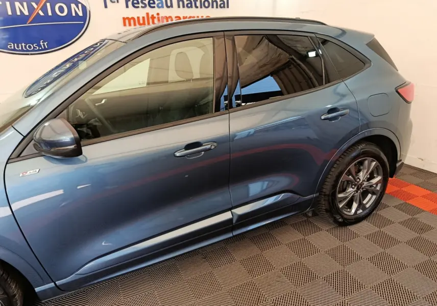 Vue latérale côté gauche d'un Ford Kuga bleu 2024 finition ST Line avec jantes alliage et rétroviseur électrique.