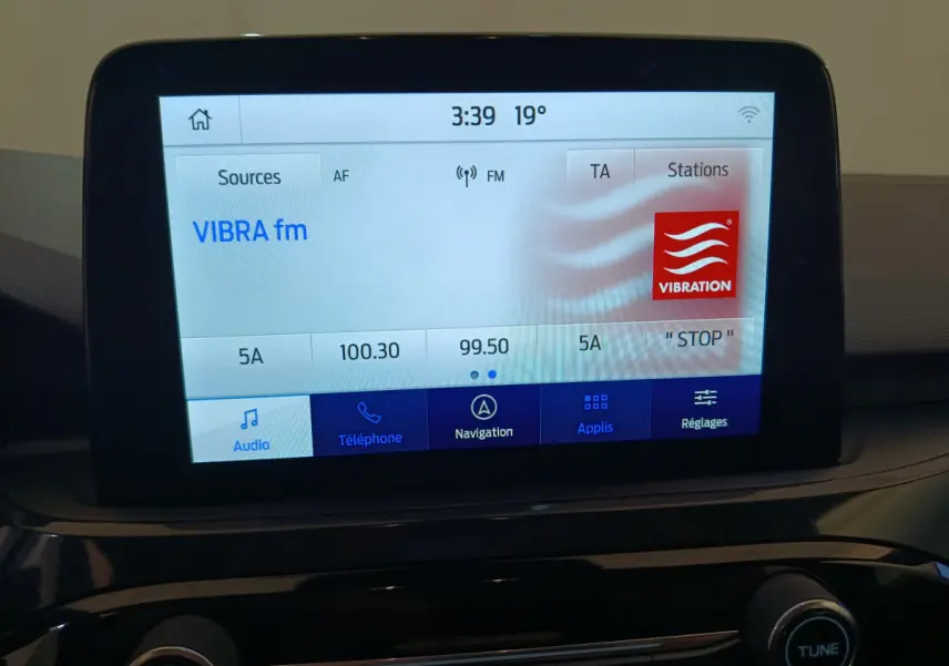 Écran tactile central du tableau de bord du Ford Kuga bleu 2024 affichant la radio VIBRA fm à 3:39 et 19°C