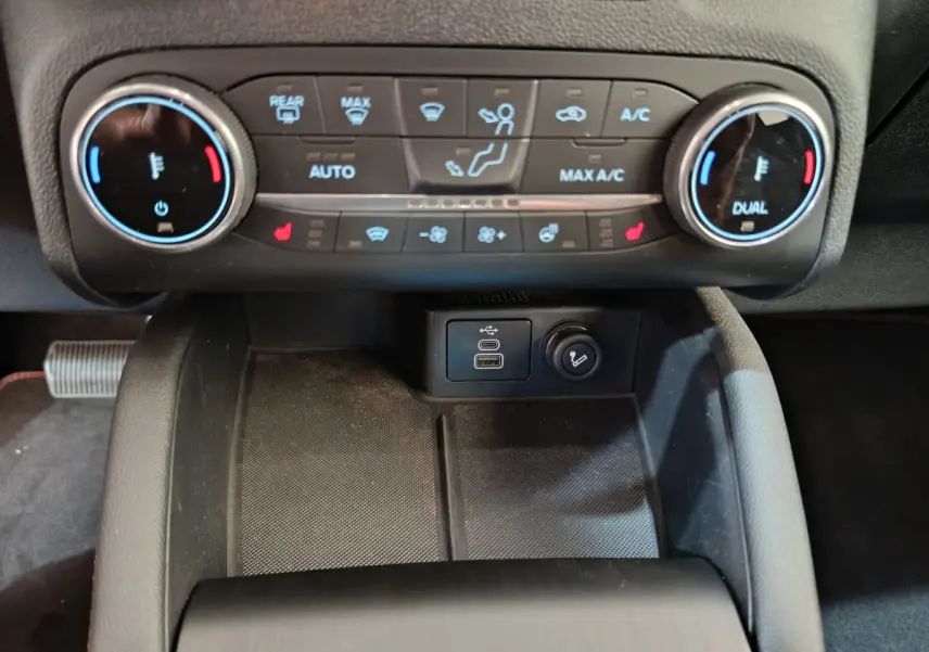 Vue rapprochée du tableau de bord central noir du Ford Kuga 2024, montrant les commandes de climatisation et ports USB.