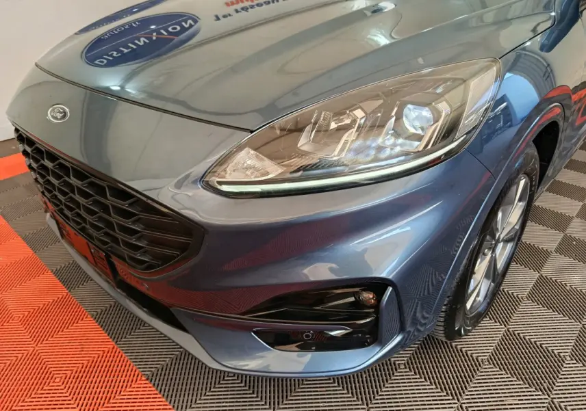 Gros plan sur l'avant droit du Ford Kuga bleu 2024, mettant en valeur le phare LED et la calandre noire.